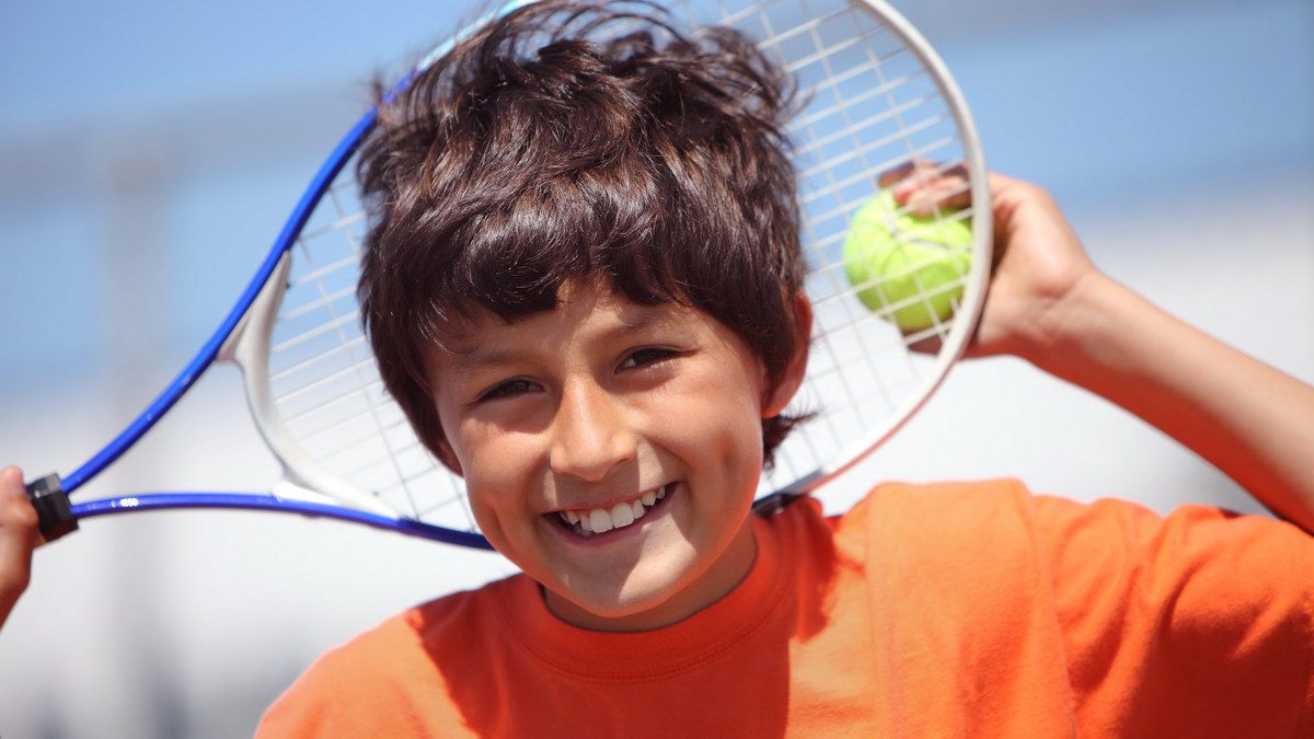 Young boy outside in sun with tennis racquet and ball - portrait